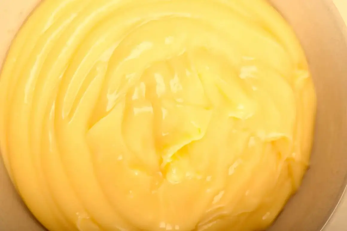 Close-up of smooth, creamy yellow pastry cream in a bowl, with visible swirls and highlights.