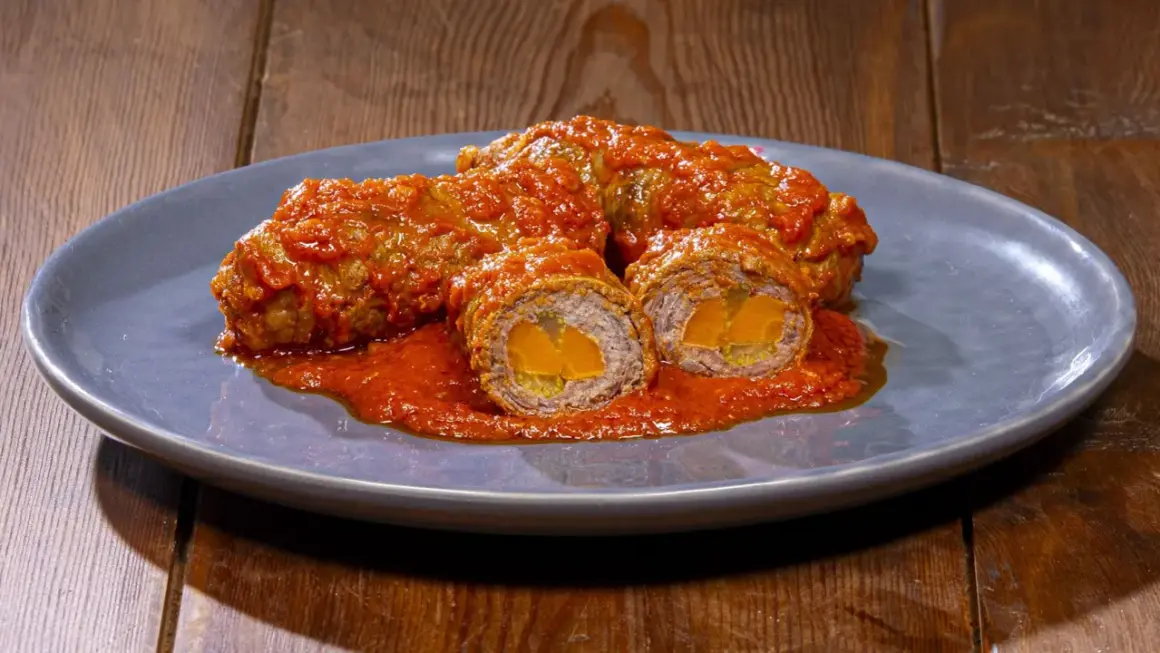 Involtini alla romana succulenti, avvolti in un sugo rosso intenso, con un cuore dorato visibile in sezione.