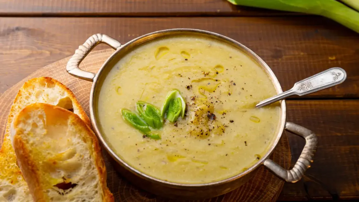 Una ciotola di cremosa crema di patate, guarnita con cipollotto fresco e pepe nero, servita con fette di pane tostato.