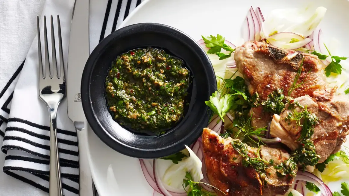 Costolette d'agnello con salsa verde senza uovo, servite su un letto di finocchio e cipolla rossa.