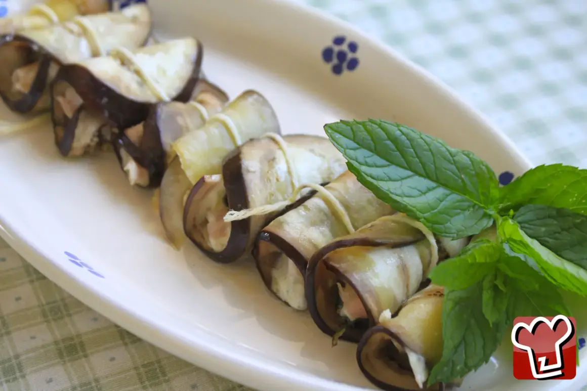 Deliziosi involtini di melanzane ripieni, guarniti con foglie di menta fresca su un piatto bianco.