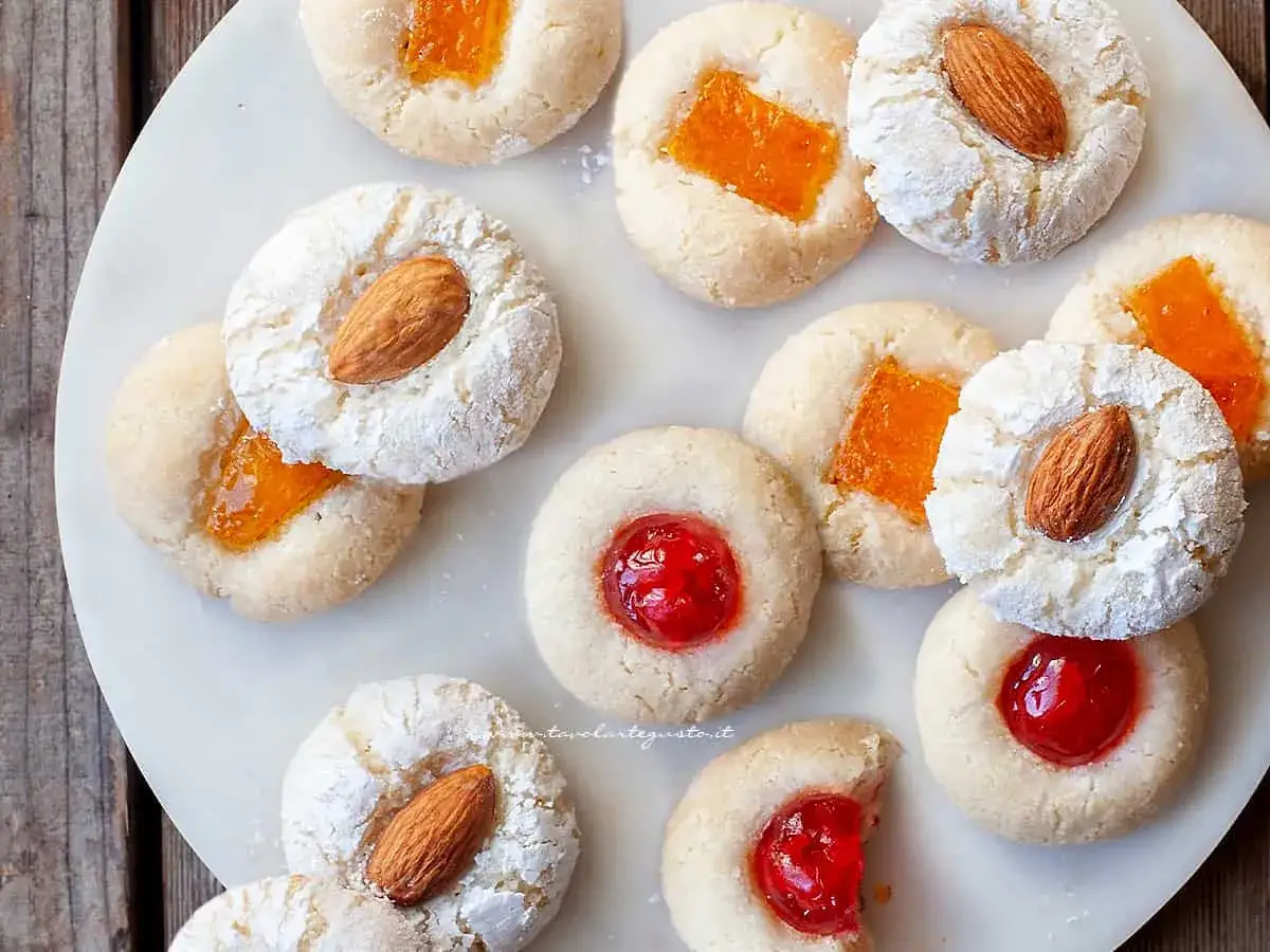 Deliziosi biscotti alle mandorle, alcuni con marmellata d'arancia, altri con ciliegina candita, spolverati di zucchero a velo.