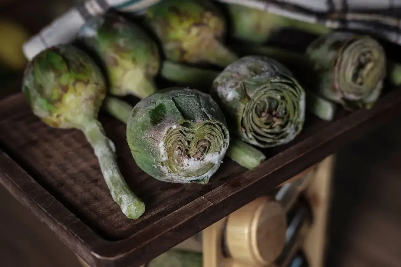 Carciofi freschi su un tagliere di legno, pronti per imparare come congelare i carciofi e conservarli per l'inverno.