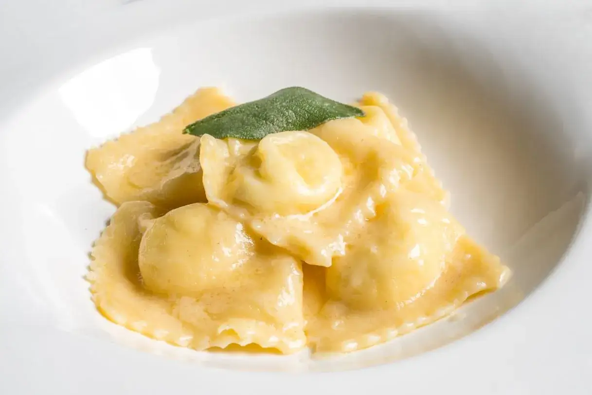 Ravioli fatti in casa, soffici e dorati, immersi in una cremosa salsa al burro e salvia, un piatto che profuma di tradizione.