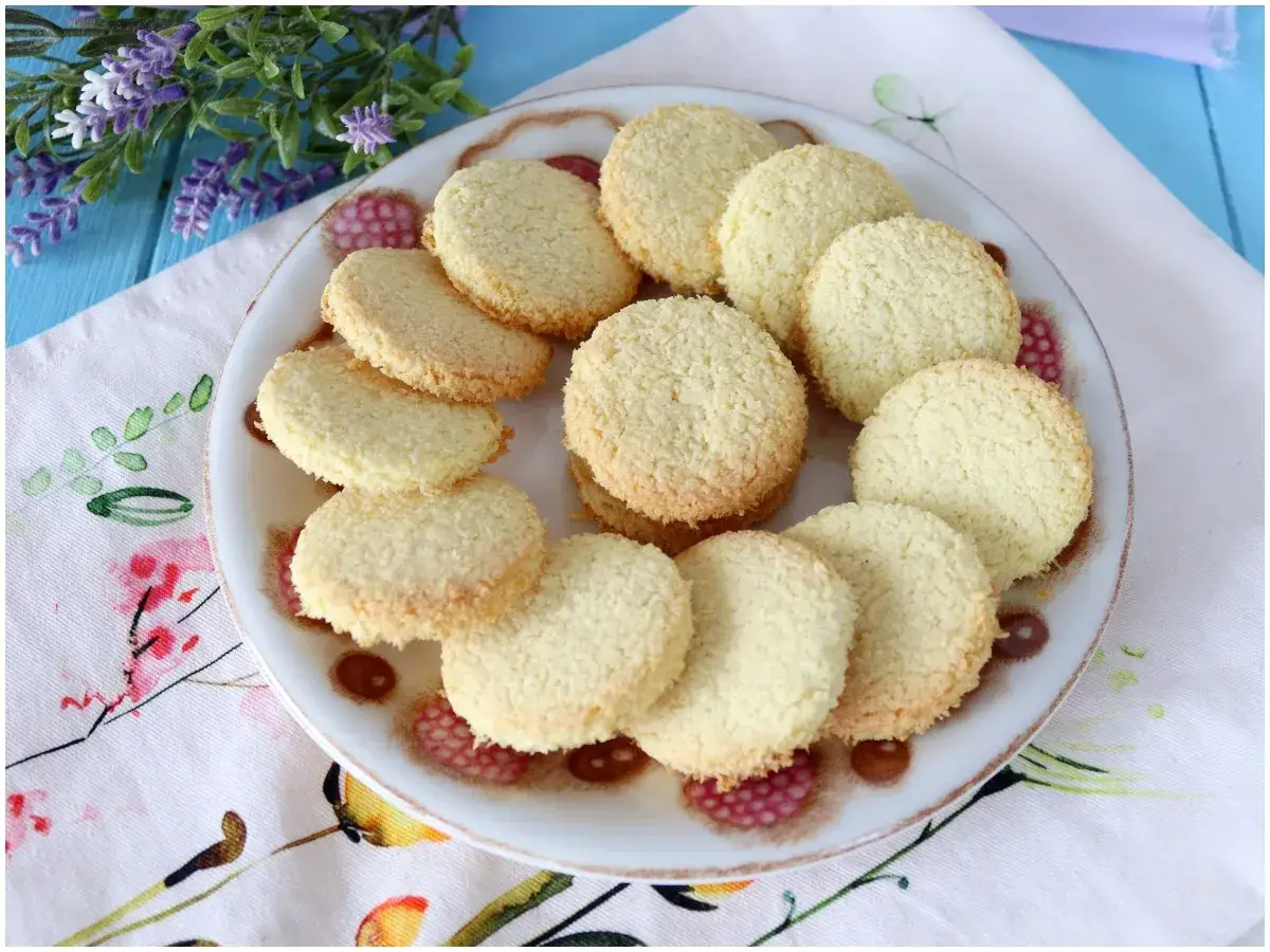 Piatto di biscotti al cocco dorati, disposti su un tovagliolo fiorato.