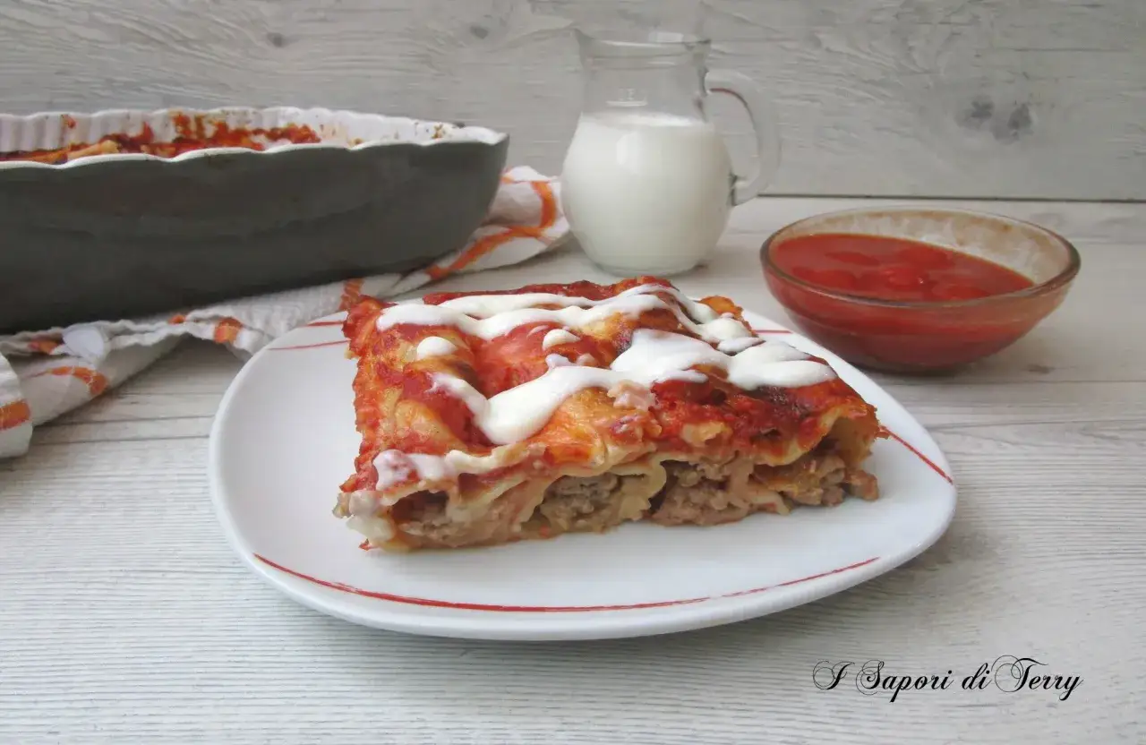 Un piatto di cannelloni ripieni di carne macinata e mozzarella, conditi con sugo rosso e una spolverata di formaggio fuso.