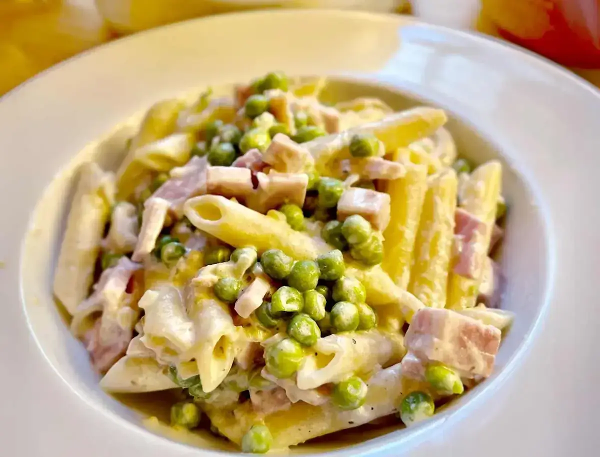 Penne cremose con piselli e prosciutto, condite con panna da cucina. Un piatto semplice e gustoso.