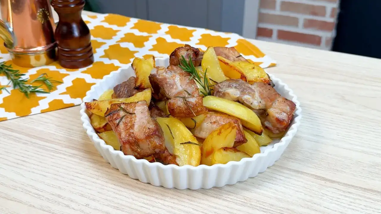 Puntine di maiale croccanti e patate al forno, profumate al rosmarino, servite in una ciotola bianca.