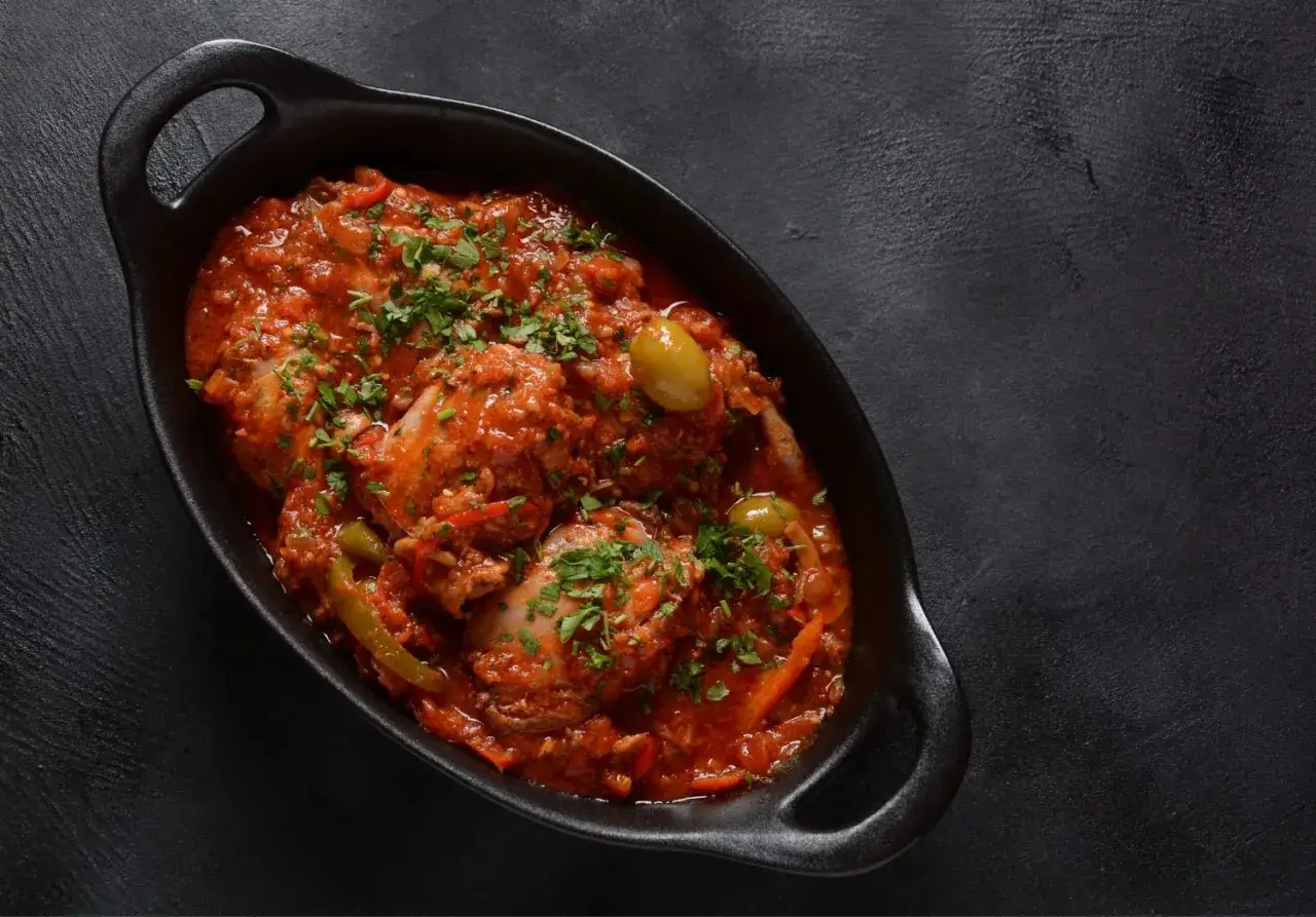 Pollo alla cacciatora ricetta della nonna: succulento pollo in umido con pomodoro, olive e erbe aromatiche, servito in una cocotte nera.