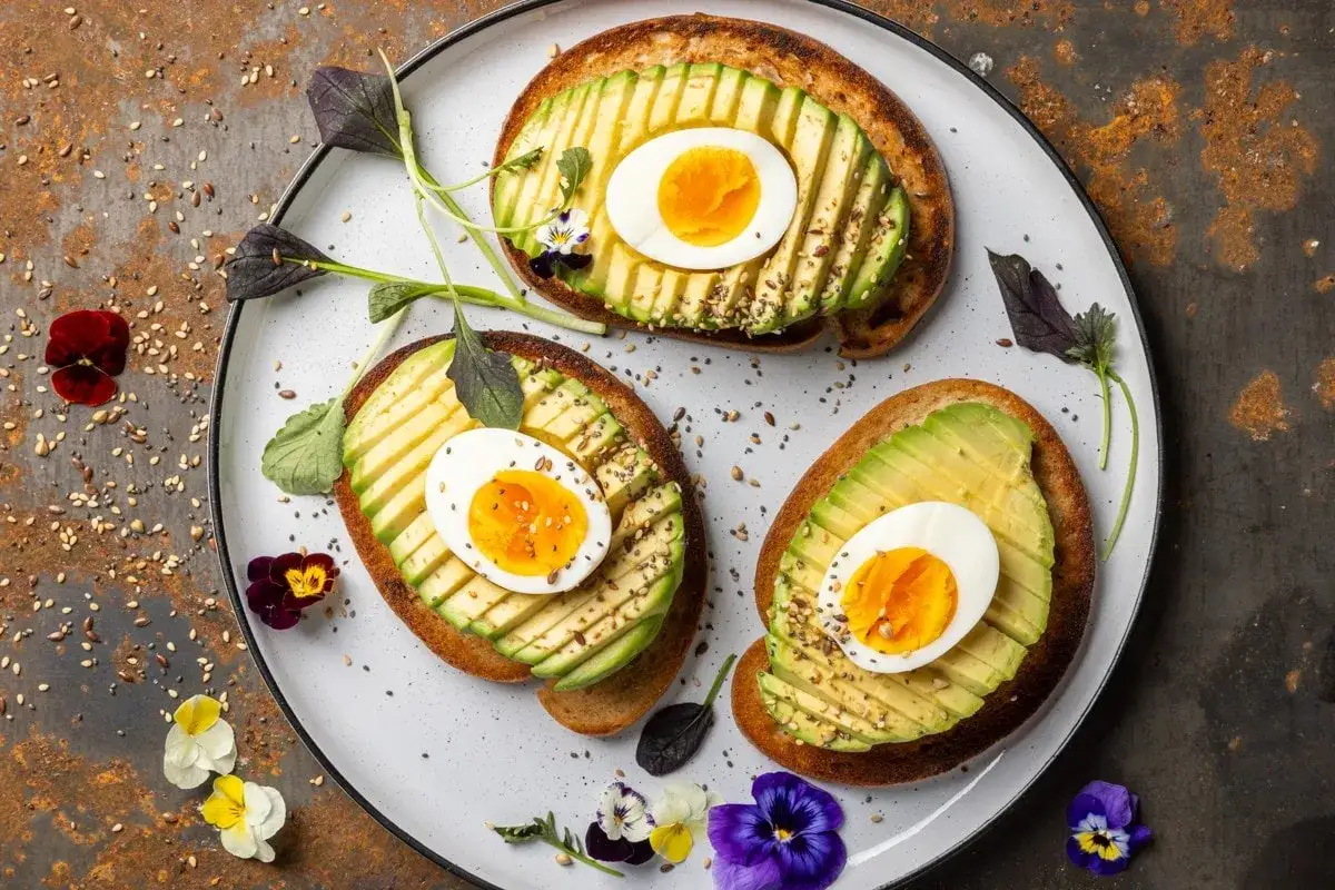 Toast con avocado e uovo sodo, un'idea per ricette con avocado veloci e gustose. Guarnito con fiori eduli e semi.