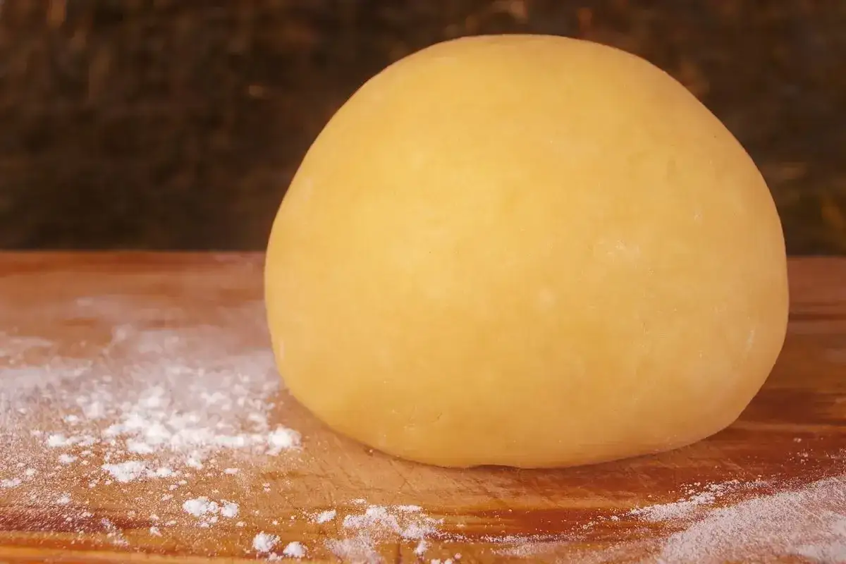 Palla di pasta frolla per pastiera su un tagliere di legno, con un po' di farina sparsa.