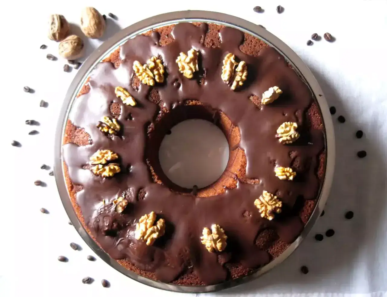 Torta al caff&egrave; con glassa al cioccolato e noci, circondata da chicchi di caff&egrave; e noci intere.