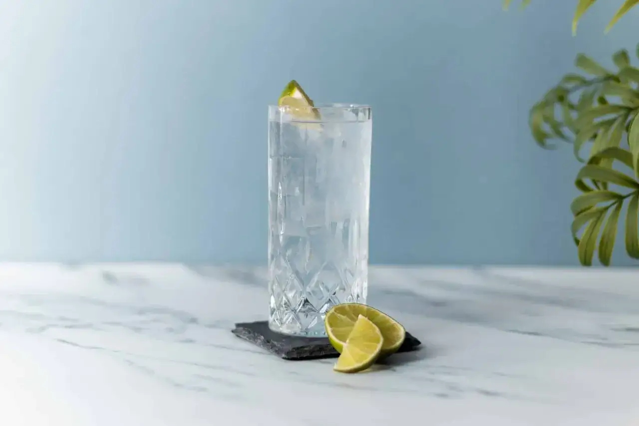 Un bicchiere di gin tonic con ghiaccio e spicchi di lime, pronto per essere gustato. La ricetta perfetta per un aperitivo rinfrescante.