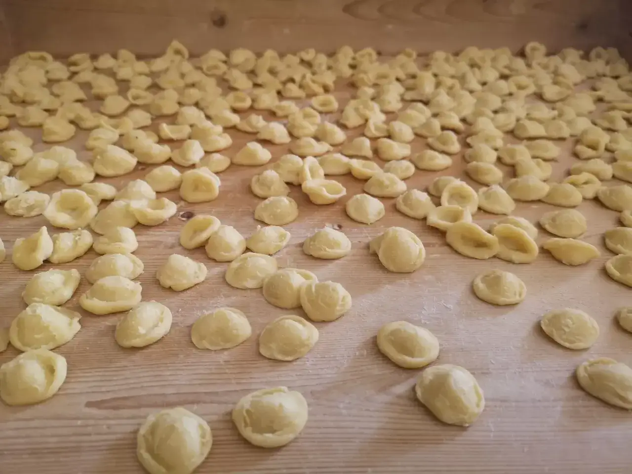 Tante orecchiette fatte in casa, pronte per essere cucinate, disposte su un tagliere di legno.