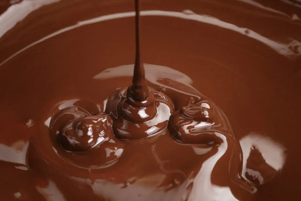 Cioccolato fuso che cola, creando forme morbide e lucide. Un invito a scoprire come sciogliere il cioccolato per dolci perfetti.