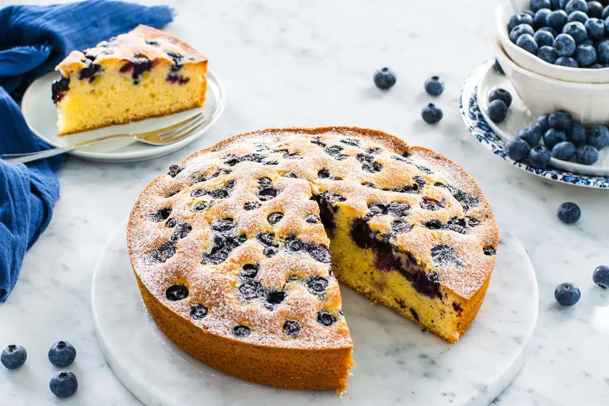 Torta 7 vasetti soffice e profumata, con mirtilli freschi e zucchero a velo. Una fetta invitante attende di essere gustata.