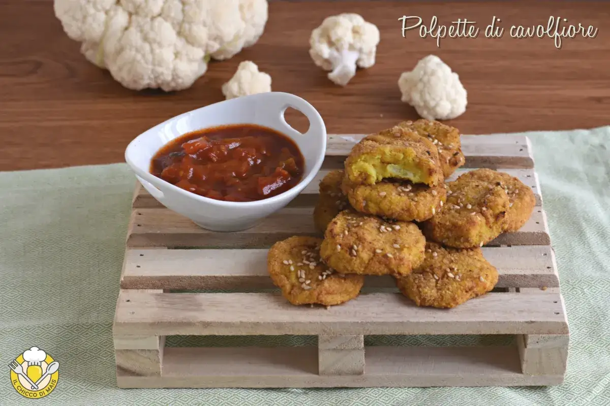 Polpette di cavolfiore dorate e croccanti, servite con salsa rossa e cavolfiore fresco sullo sfondo.