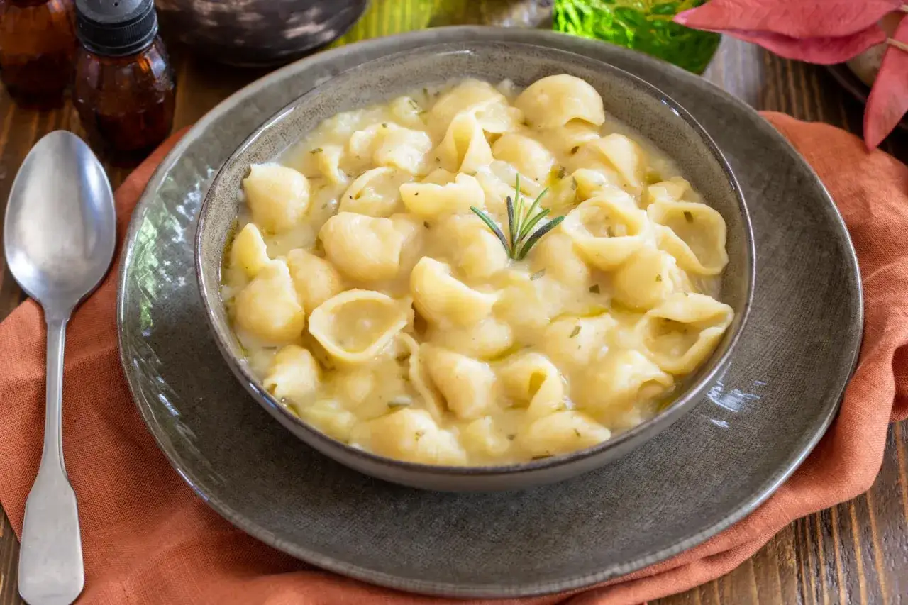 Una ciotola fumante di pasta e patate cremosa, guarnita con rosmarino fresco. Un piatto confortante pronto per essere gustato.