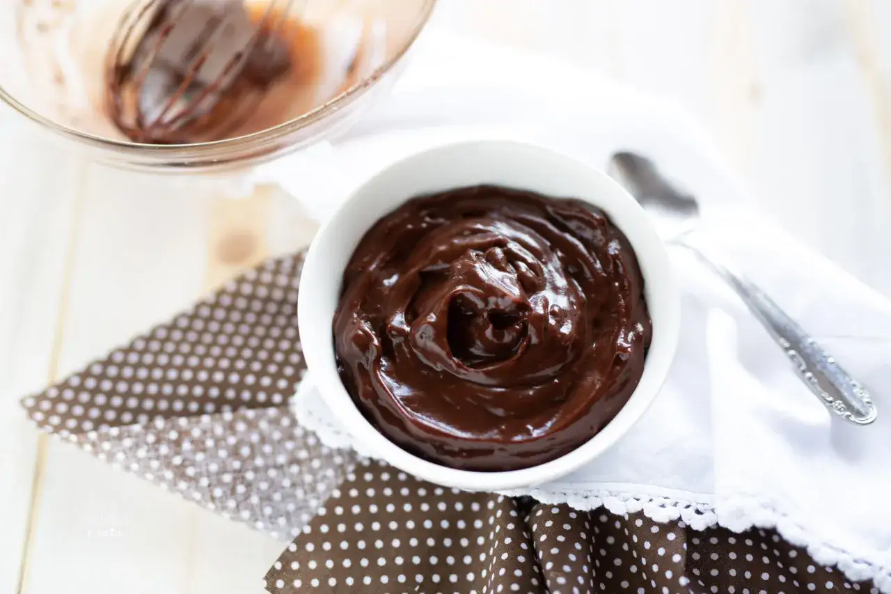 Una ciotola bianca piena di lucida crema al cioccolato, pronta per essere gustata.
