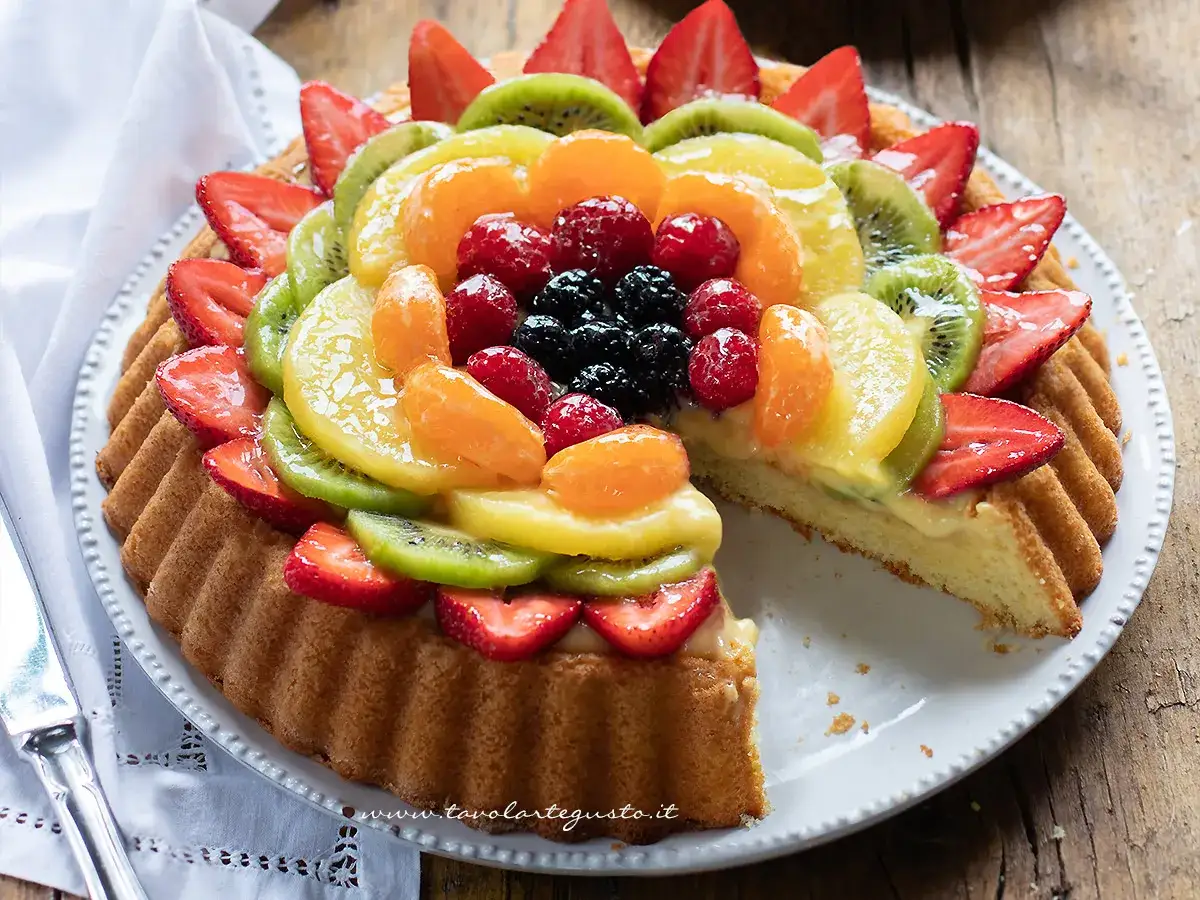 Pan di spagna decorato con frutta fresca: fragole, kiwi, mandarini, lamponi e mirtilli.