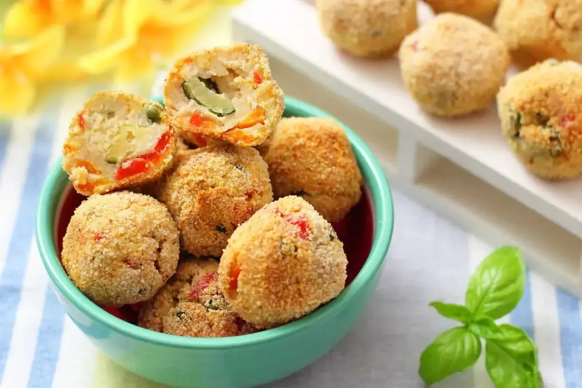 Polpette di zucchine e ricotta dorate e croccanti, piene di verdure colorate, servite in una ciotola turchese.