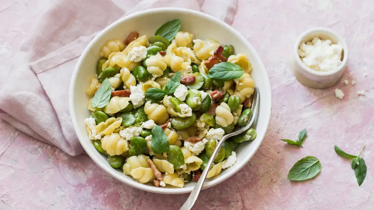 Un piatto invitante di pasta e fave, arricchito da cubetti di formaggio fresco e guarnito con foglie di menta.