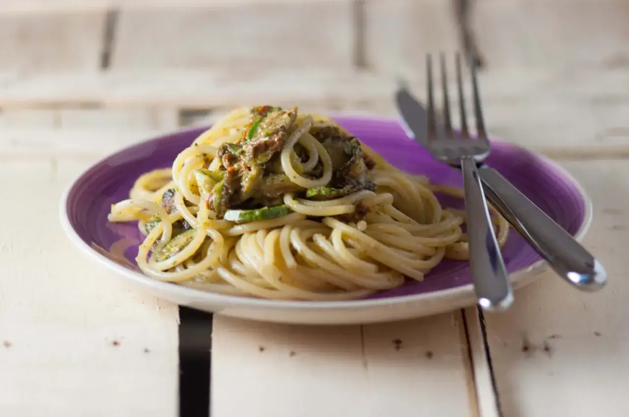 Spaghetti con carbonara di zucchine, un piatto leggero e gustoso, servito su un piatto viola con forchetta e coltello.