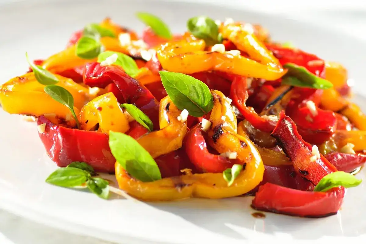 Peperoni arrostiti, rossi e gialli, conditi con aglio e basilico fresco. Un'idea gustosa per le tue ricette con peperoni.