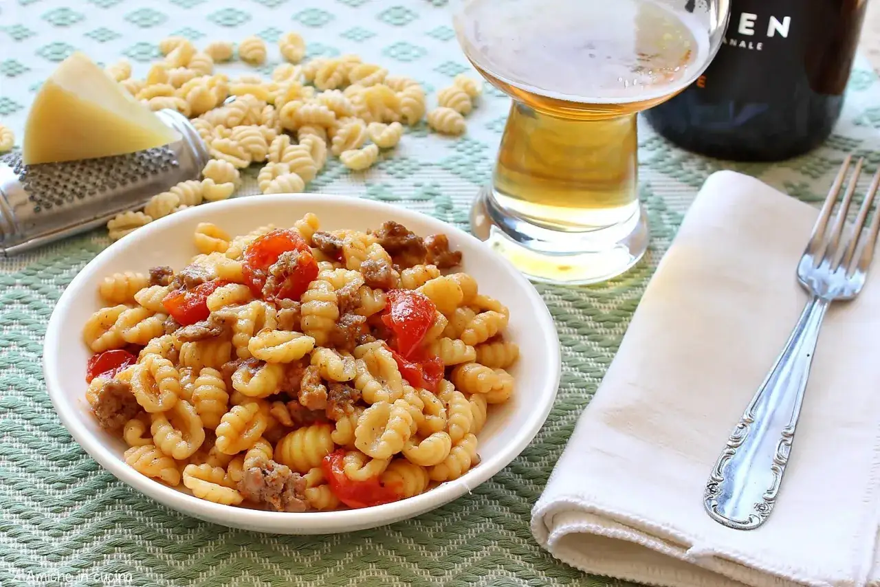 Un piatto di malloreddus alla campidanese, con salsiccia e pomodorini, pronto per essere gustato con una birra.