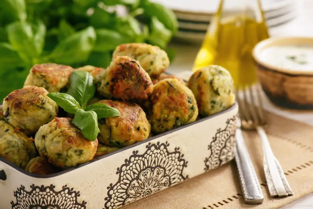 Polpette di zucchine al forno dorate e profumate, guarnite con basilico fresco, pronte per essere gustate.