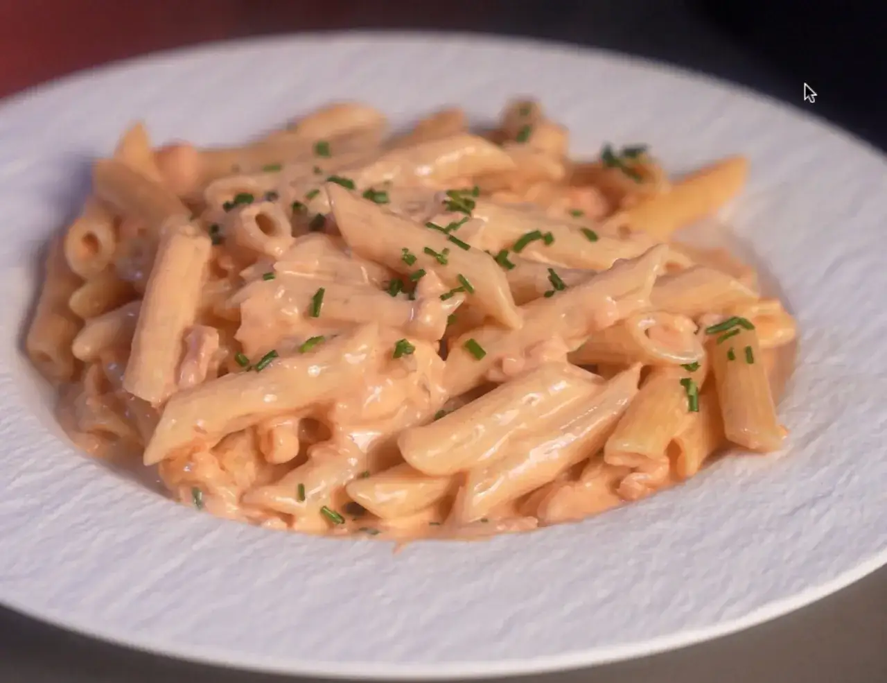 Penne alla vodka cremose e saporite, guarnite con erba cipollina fresca, servite su un piatto bianco texturizzato.