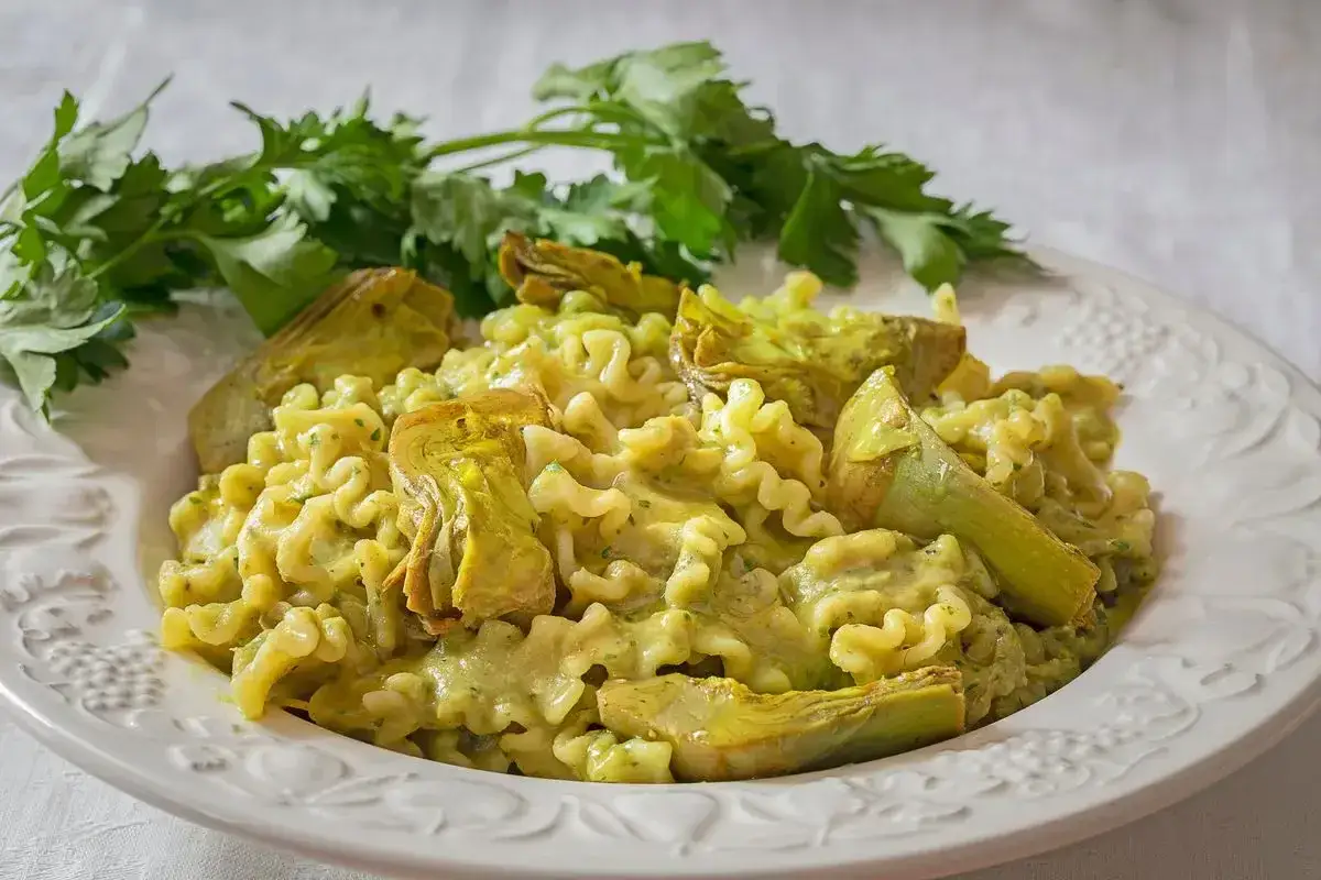 Pasta con crema di carciofi e pezzi di carciofo fresco, guarnita con prezzemolo.