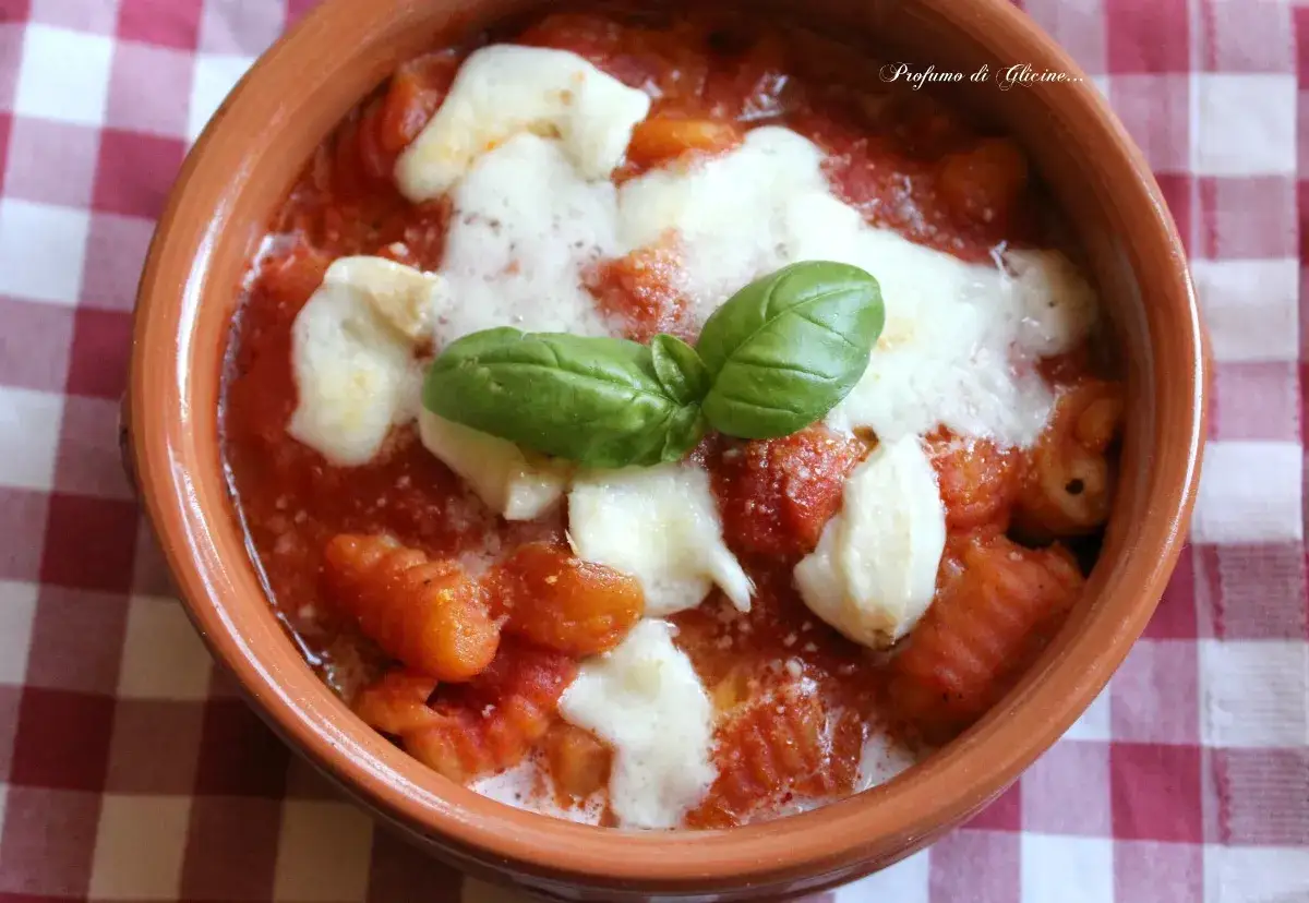 Gnocchi alla sorrentina fumanti in terracotta, con mozzarella filante e basilico fresco. Un classico della cucina italiana.