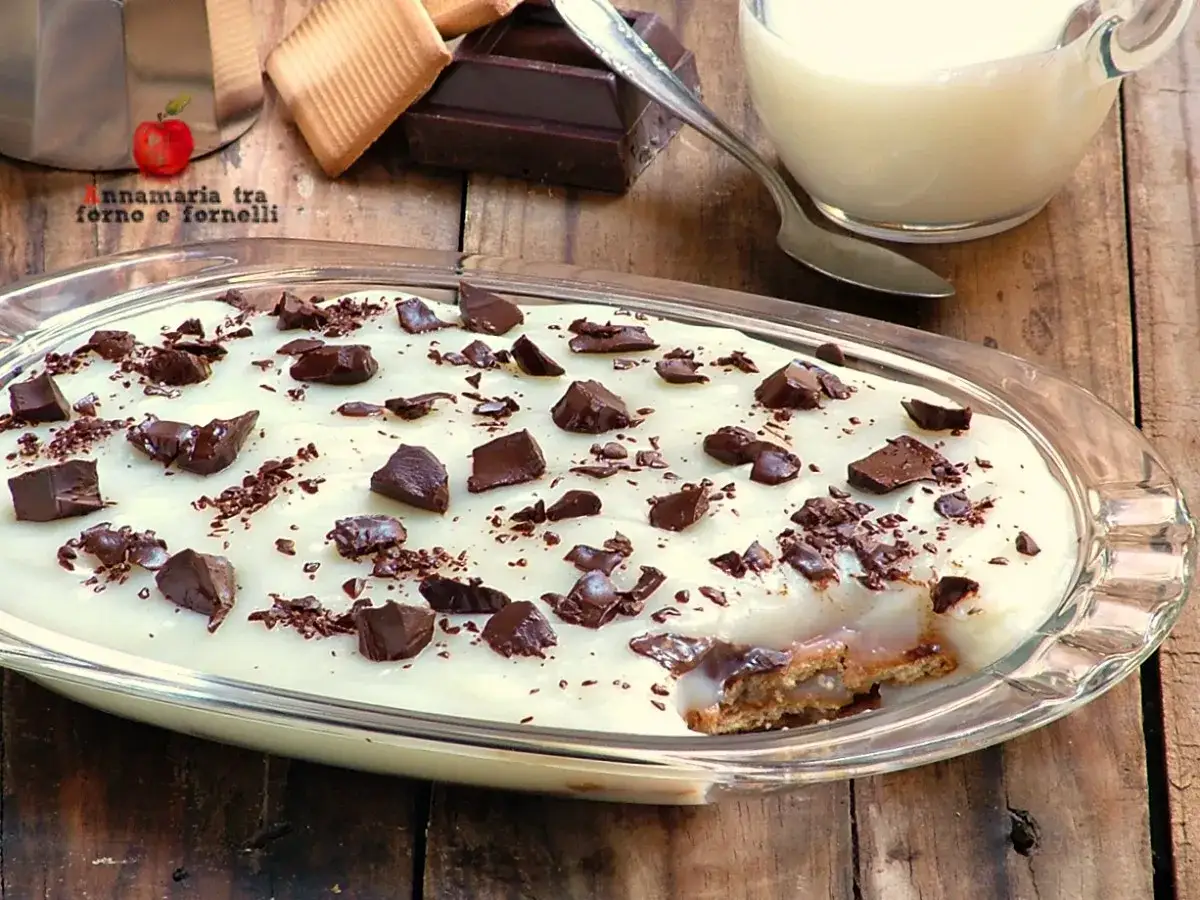 Dolce al cucchiaio con crema chiara, ricoperto di cioccolato fondente a pezzi e scaglie. Sotto, biscotti e un velo di dulce de leche.
