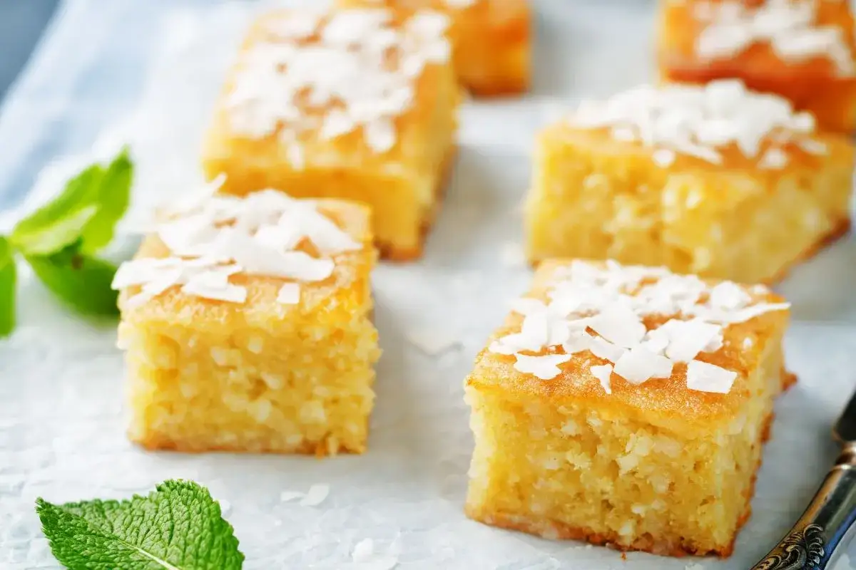 Fette di torta al cocco, dorate e soffici, guarnite con scaglie di cocco e foglioline di menta fresca.