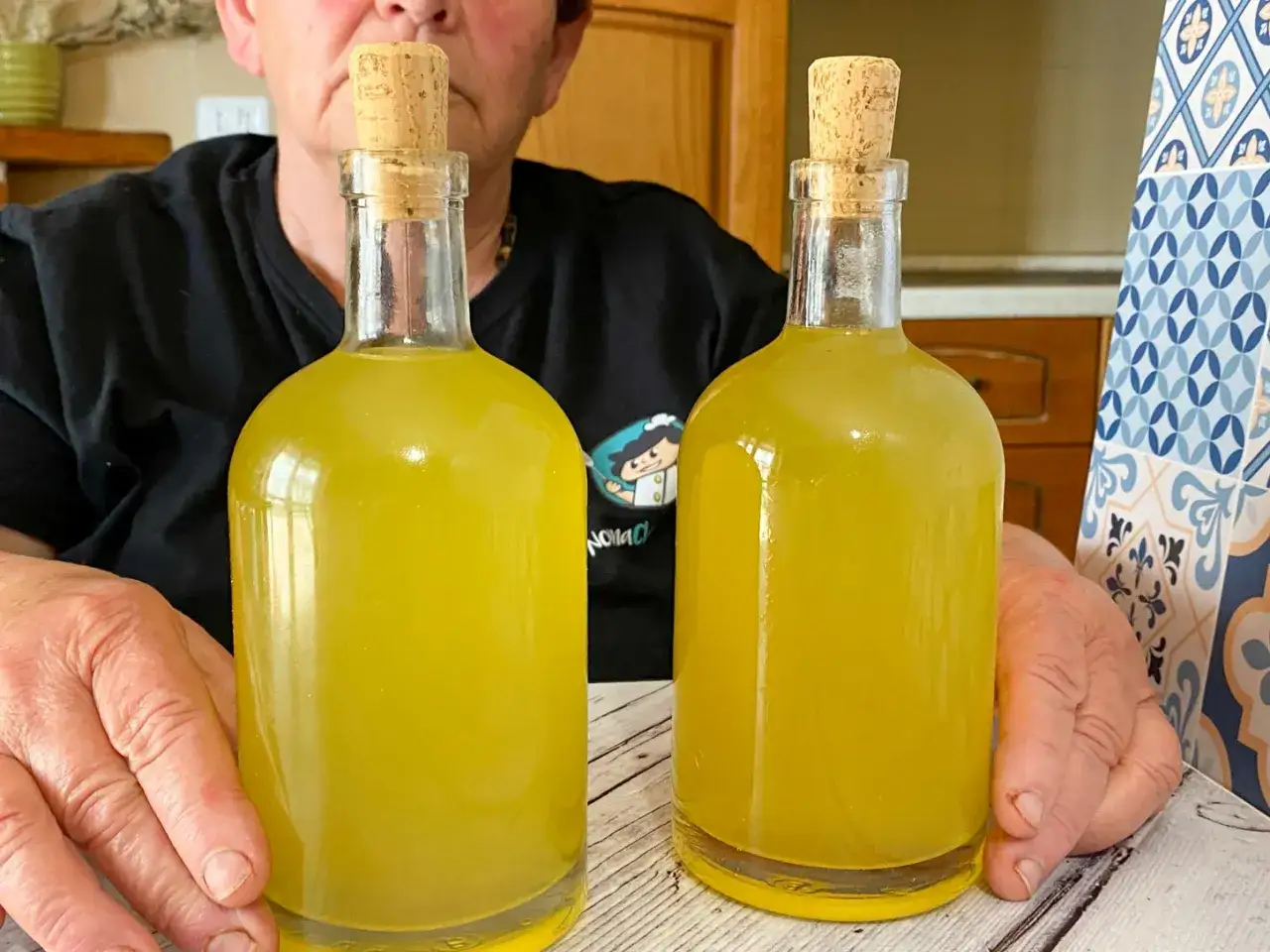 Due bottiglie di limoncello fatto in casa, un classico per la ricetta limoncello 1 litro alcool. Le mani di una nonna sorreggono i contenitori.