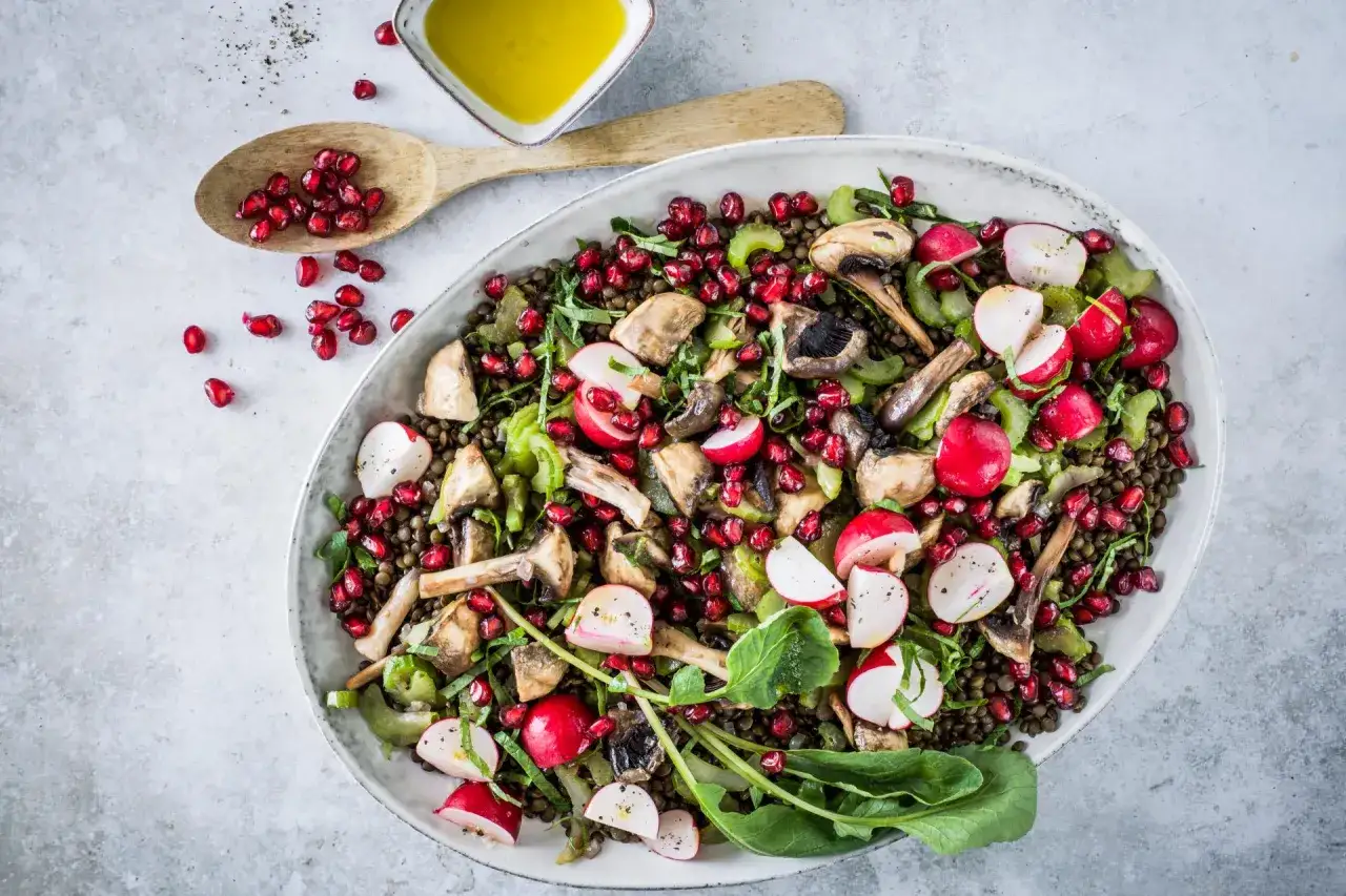 Un'insalata di lenticchie colorata con ravanelli, funghi, sedano e chicchi di melograno, condita con olio d'oliva.