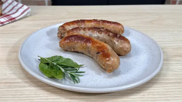 Tre succulente salsicce dorate in padella, servite su un piatto con rosmarino e alloro.