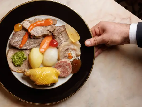 Piatto ricco con bollito di carne, pollo, salumi, verdure e salse, servito su un piatto elegante.