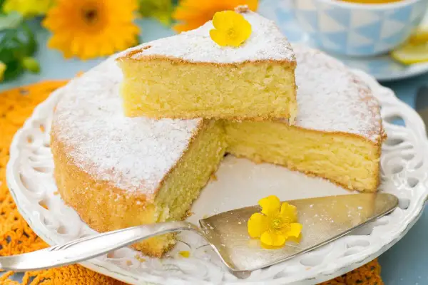 Una torta paradiso sofficissima, spolverata di zucchero a velo e decorata con un fiore giallo, pronta per essere gustata.