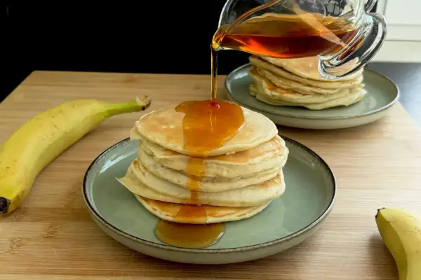 Pancake alla banana con sciroppo d'acero che cola su una pila di soffici pancake.