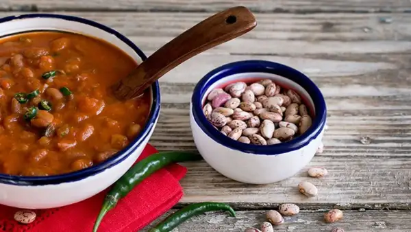 Un piatto fumante di fagioli alla messicana, con peperoncini verdi e una ciotola di fagioli crudi, pronti per un sapore piccante.
