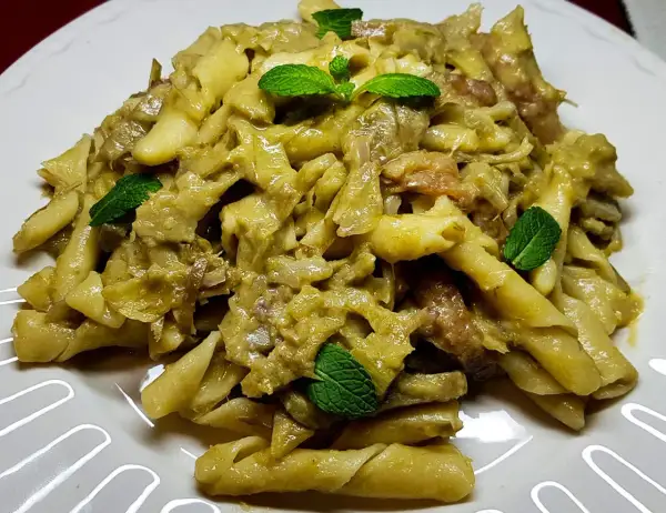 Pasta con carciofi alla siciliana, un piatto saporito e profumato, guarnito con foglie di menta fresca.