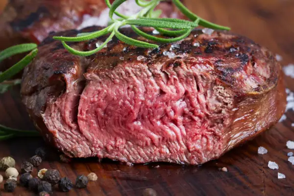 Succulenta tagliata di manzo al sangue, guarnita con rosmarino fresco e sale grosso, su un tagliere di legno.