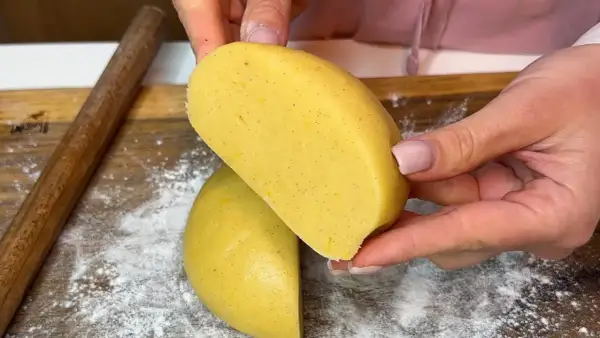 Mani che tengono un impasto giallo, profumato alla vaniglia, pronto per diventare una deliziosa pasta frolla senza burro.