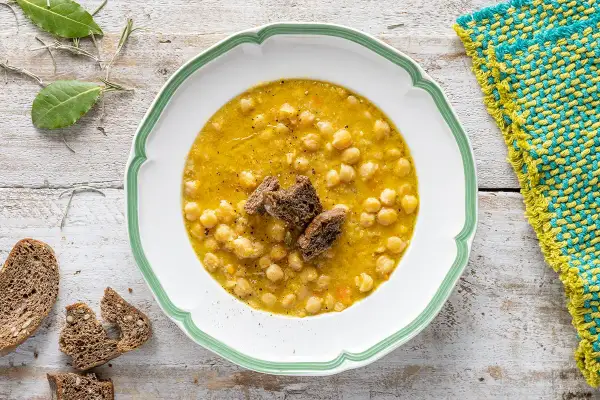 Un piatto invitante di zuppa di ceci, guarnito con crostini di pane scuro e accompagnato da fette di pane integrale.