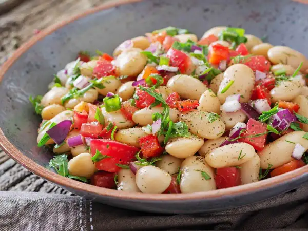 Insalata di fagioli bianchi, pomodori, cipolla rossa e erbe fresche, condita con spezie. Un piatto colorato e gustoso.