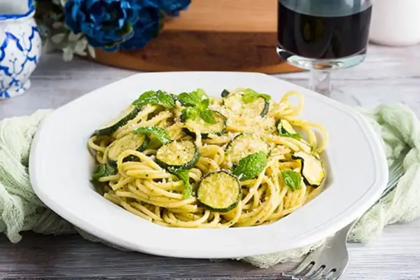 Un piatto di spaghetti con zucchine e menta fresca, un classico della pasta e zucchine alla siciliana, guarnito con parmigiano grattugiato.