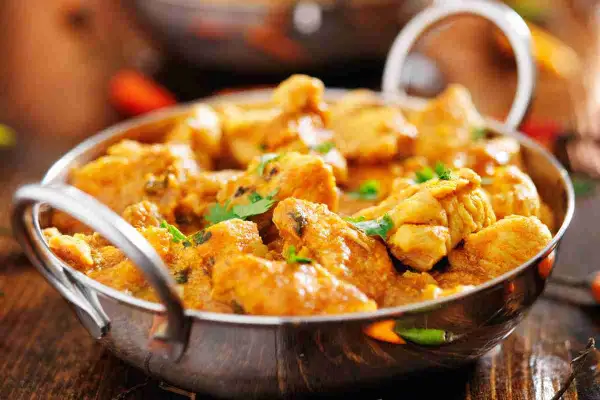 Un invitante pollo al curry cremoso, guarnito con coriandolo fresco, servito in una ciotola metallica su un tavolo di legno.