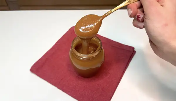 Un cucchiaio d'oro raccoglie un cremoso dulce de leche da un vasetto su un tovagliolo rosso.